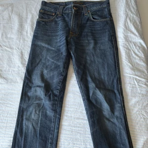 Blå jeans från Nudie Jeans, W30 L32 - Snygga blå jeans från Nudie Jeans med klassisk femficksdesign och coola kontrastsömmar. Modellen har raka ben och normal passform, med Nudie-logga på bakfickan och läderpatch i midjan. Perfekt för dig som gillar stilrena och tidlösa jeans.