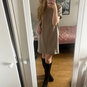 Beige t-shirtklänning i bomull strl S - Enkel beige t-shirtklänning med rund hals och korta ärmar. Klänningen har en rak passform. Perfekt att styla med boots eller sneakers😍Materialet är mjukt och klänningen har inte använts mer än att prövats. 