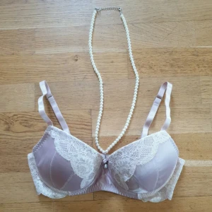 Ljuslila spets BH med pärldetalj - Supersnygg ljuslila BH med mjuk spets i vitt och pärldetalj framtill. Axelbandslös design med justerbara band och silkeslen satinfinish. Notera, sytt på ena sidan ca 1cm, se bild. Använd 2 ggr sedan tvättad. Storlek 75B