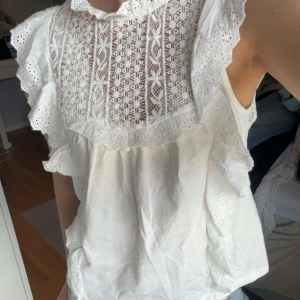 Vit blus med spets och volanger - Superfin blus🤍🤍 har dessvärre två små defekter därav priset, men ingen av de är något man tänker på. En liten fläck vid ena volangen (se bild två) & en liten smink fläck på insidan av halsen (se bild tre, inget som syns när den bärs då det är på insidan)