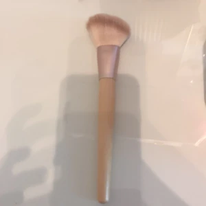 Stor fluffig sminkborste med trähandtag - Säljer en stor och mjuk sminkborste med ljust trähandtag och roséguldfärgat metallfäste. Borsten har täta, ljusbruna syntetiska strån och är perfekt för applicering av puder, bronzer eller rouge. Enkel att hålla i och ger ett jämnt resultat.