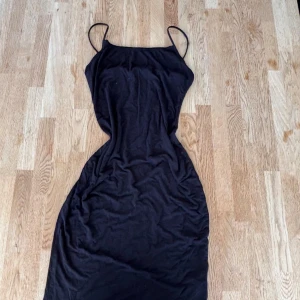 Svart långklänning med smala axelband - Snygg svart långklänning med smala axelband och figurnära passform. Klänningen har en enkel och stilren design som ger en cool och modern vibe. Perfekt för dig som gillar minimalistiskt mode och vill ha en klänning som är lätt att styla.