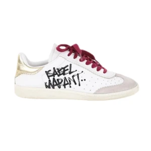 Isabel Marant sneakers med röda snören - Snygga vita sneakers från Isabel Marant med cool svart graffiti-logga på sidan, röda snören och guldiga detaljer vid hälen. Skorna har rund tå, platt sula och inslag av mocka framtill. Perfekt för dig som gillar unika detaljer. Lite slitna på lädret, kolla bild 4☺️