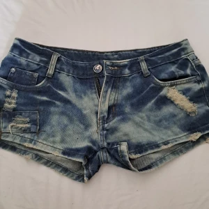 Blåa low waist jeans shorts - Snygga low waist jeansshorts som är väldigt korta. Slitna detaljer och har många nyanser av blå. Köpt från en marknad i Thailand.