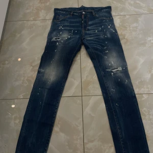 Dsquared2 blå skinny jeans med detaljer - Snygga blå jeans från Dsquared2 i skinny fit med coola slitningar och färgstänk på både fram- och baksida. Jeansen har klassiska fem fickor, dragkedja och unika broderade detaljer på bakfickorna. Perfekt för dig som gillar streetstyle och vill sticka ut.