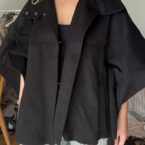 Trekvartsärmad kappa - Svart kappa från H&M med trekvartsärmad och lite poncho-modell. Jackan har en oversized passform och är tillverkad i mjukt ullmaterial.
