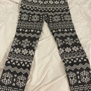 Svarta fodrade leggings med vintermönster - Säljer ett par svarta leggings med vita snöflingor, hjärtan och geometriska mönster. De har hög midja och är stickade i mjukt material, perfekta för kalla dagar. Passar dig som gillar mysiga och snygga vinterplagg med lite extra stil.