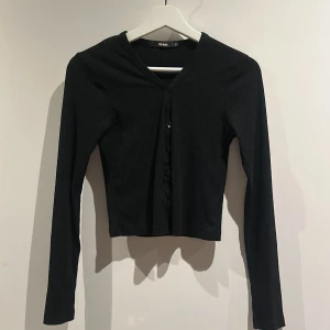 Svart ribbad kofta från Bik Bok - Svart ribbad kofta från Bik Bok i storlek XS. Croppad modell med v-ringning och knappar framtill. Långärmad och i mjukt, stretchigt material. 