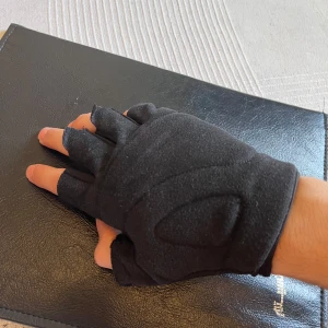 Svarta fingerlösa träningshandskar 2st(högerhand) - Säljer ett par svarta fingerlösa träningshandskar med vadderad ovansida och smidig passform. Handskarna har kardborre vid handleden och är gjorda i syntetmaterial med stretch. Perfekta för gymmet eller cykling, och har diskreta vita detaljer på ovansidan.