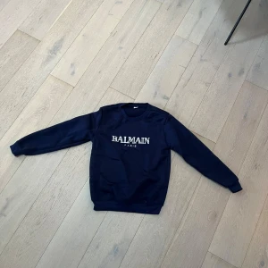 Mörkblå sweatshirt från Balmain passar S  - Snygg mörkblå sweatshirt från Balmain Paris med vit logotyp på bröstet. Tröjan har rund hals och långa ärmar, perfekt för dig som gillar stilrena och exklusiva märken. Passar dig som vill ha en enkel men lyxig look.