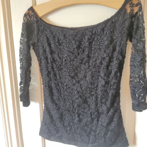 Svart spetstopp - Svart tooo i spets med trekvartsärm. Själva kroppen av tröjan är täckt i spets men har ett svart under tyg medan ärmarna endast är i spets. Den är nog menad att ha off the shoulder eller typ på axeln så den får en vid urringning. 