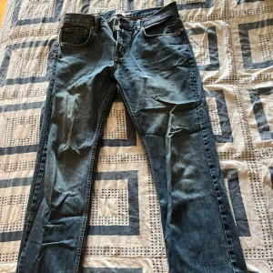 Lager 157 blå jeans straight fit - Säljer ett par lager 157 jeans i blå denim med straight fit. De har fem fickor, bälteshällor och en snygg tvättad look. Passar dig som gillar tidlös stil och vill ha jeans med lite längre ben och normal passform.