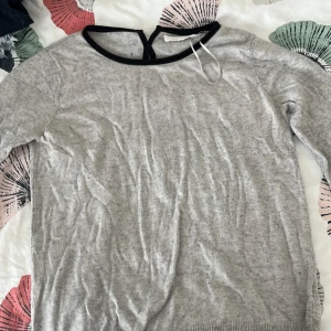 Grå stickad tröja med svarta rosetter - Supersöt grå stickad tröja från Grace & Mila i storlek M. Tröjan har svarta detaljer runt halsen och tre svarta rosetter på ryggen som ger en unik touch. Långärmad och mjuk, perfekt för dig som gillar stilrena men ändå lekfulla plagg. Funkar även om du är en storlek S!! Priset kan även diskuteras❣️❣️