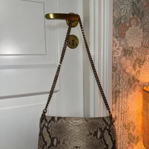  Zadig & Voltaire Rock leather crossbody bag - Zadig & Voltaire Rock bag i ormmönster, inköpt 2017/2018 (nypris 4 000–5 000 kr). Poppis och tidlös modell med flera fack och axelkedja. Säljs med korta axelkedjan, den längre crossbody-kedjan är trasig men går att ersätta. Skick: väl använd med lite slitage, t.ex invändiga bläckfläckar i ena facket (bild 4) dessa syns inte utvändigt , mindre hål på utsidan, inte i själva facket! (bild 3), samt viss rost på kedjor (ej funktionspåverkan). Fullt användbar. Pris: 1 200 kr (eller högstbjudande).