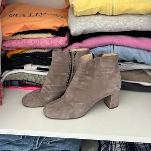 Beige mocka boots från Rizzo - Snygga boots i beige mocka från Rizzo, tillverkade i Italien. Skorna har en rund tå, blockklack och coola dragkedjor med ringdetalj på sidan. Insidan är fodrad i ljust skinn för extra komfort. Perfekt för dig som gillar stilrena och trendiga detaljer.