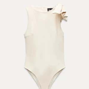 body med rosett - Supersnygg beige bodysuit från Zara med en stor rosett på axeln. Modellen är ärmlös och har en clean, slim passform som sitter tajt mot kroppen. Perfekt att styla med jeans eller kjol för en chic look. Materialet känns mjukt och har en lätt glans.