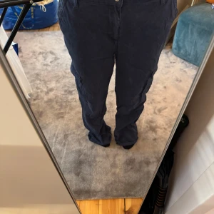 Mörkblå cargopants med raka ben - Säljer ett par mörkblå cargopants med raka ben och flera praktiska fickor på sidorna. Byxorna har normal passform och midwaist, tillverkade i mjukt bomullsmaterial. Perfekt för dig som gillar en avslappnad och cool stil.