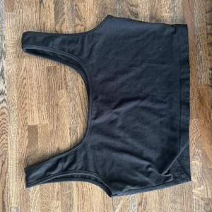 Svart croppad linnetopp från SHEIN - Svart croppad linnetopp från SHEIN i mjuk bomullsmix. Toppen har breda axelband och är ärmlös med en enkel, stilren design. Perfekt att matcha med höga jeans eller shorts för en chill look.