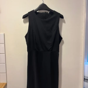 Svart ärmlös långklänning - Snygg svart långklänning med klassisk rund halsringning och ärmlös design. Klänningen har en diskret dragkedja i ryggen och är tillverkad i ett mjukt, slätt material som faller fint. Perfekt för dig som gillar stilrena och tidlösa plagg.