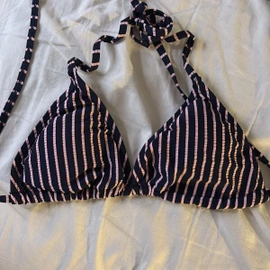 Randig bikini med snörning - Snygg bikiniöverdel med blåa och ljusrosa ränder. Klassisk trekantsmodell med knyt i nacken och ryggen för perfekt passform. Perfekt för strandhäng och poolparty. Materialet känns mjukt och följsamt mot huden.