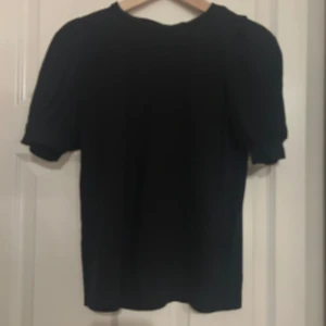 Svart puffärm topp i bomull - En svart topp med puffiga korta ärmar och rund hals. Materialet är mjukt bomullstyg som känns skönt mot huden. Enkel och stilren design som funkar till många olika looks. Perfekt om du gillar minimalistisk stil med en twist på ärmarna.