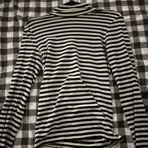 Svartvit randig polotröja - Säljer en svartvit polotröja med klassiskt horisontellt randigt mönster. Tröjan har lång ärm och en hög krage som ger en cool och stilren vibe. Perfekt att matcha med jeans eller kjol för en trendig look.