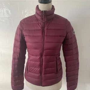 Vinröd dunjacka från Abercrombie & Fitch - Säljer en snygg vinröd dunjacka från Abercrombie & Fitch. Jackan har en dragkedja framtill och är långärmad med en hög krage. Perfekt för kyliga dagar med sin quiltade design och varma fyllning. Fick ett lite hål på insidan av jackärmen som syddes.  Se på bilder. Ej märkbart vid användning då det är nära sömn insidan av arm. 