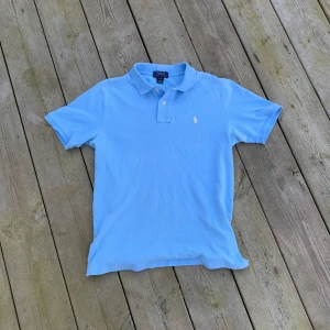 Ljusblå pikétröja från Ralph Lauren - Säljer en stilren ljusblå pikétröja från Ralph Lauren med klassisk krage och knappar. Tröjan har en broderad logga på bröstet och är kortärmad. Perfekt för en avslappnad och snygg look. 🌟