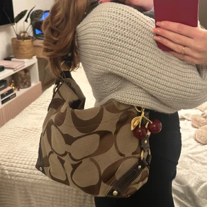 Coach Signature Carly Hobo Bag - Det gör ont att sälja den men jag använder tyvärr inte denna längre (OBS körsbär dekor är ej äkta, köpta slumpmässigt men kommer medfölja som en snygg detalj!)  Detta är en äkta Coach vintage Carly Hobo Bag. Verkligen ser inte alls använd och inga repor, därav seriös köpare! Super vacker väska som fick sitta hemma superlänge. Har läder och äkta palladium guld som inte blir alls grön. En gammal certifikat medföljer. 