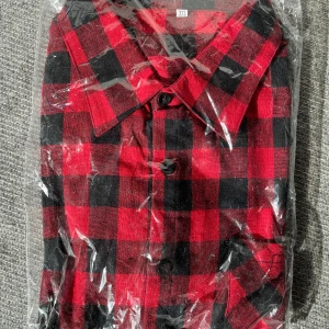 Röd och svart rutig skjorta - Snygg röd och svart rutig skjorta med klassisk krage och knappar framtill. Skjortan är långärmad och passar bra till både jeans och chinos.