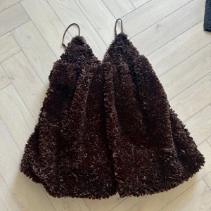 Brun klänning med volangdetaljer - Säljer en unik brun klänning med volangdetaljer och tunna axelband. Testad men inte använd. Perfekt för en speciell kväll med sin texturerade look och eleganta design.