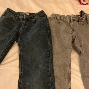 Jeansbyxor från Lindex - Två par jeansbyxor från Lindex i olika nyanser. Ett par är mörkblå och det andra är grå. Båda har klassisk femficksdesign och är tillverkade i jeansmaterial. Perfekta för en avslappnad stil.