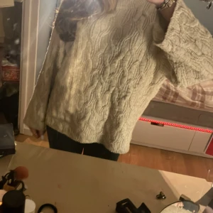 Beige stickad tröja från Monki - Säljer en mysig beige stickad tröja från Monki. Tröjan har ett snyggt kabelstickat mönster och långa ärmar. Perfekt för kyliga dagar!