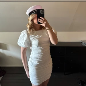 Vit klänning från Nelly (studentklänning) - Säljer en vit klänning från Nelly med puffiga kortärmar och en öppen rygg. Klänningen har en tight passform och är perfekt för sommarens festligheter. Den är stilren och elegant, vilket gör den perfekt till studenten men även andra tillfällen i sommar. (klänningen är enbart testad, etikett sitter kvar) köpare står för frakt 💞