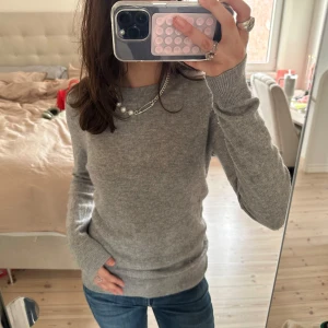 100% cashmere tröja från Indiska - Säljer grå stickad tröja från Indiska, 100% cashmere. Tröjan har en klassisk rund halsringning och långa ärmar, perfekt för kyligare dagar. Den är mjuk och bekväm men har ett litet hål (se sista bilden) som inte syns🍒❤️‍🔥