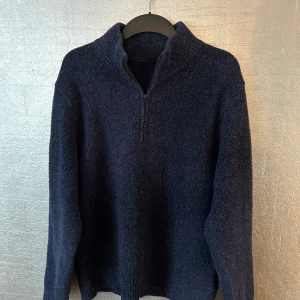 Mörkblå stickad tröja med dragkedja - Säljer en stilren mörkblå stickad tröja med halv zip. Perfekt för kyliga dagar och ger en avslappnad men ändå snygg look. Tröjan har långa ärmar och ribbade kanter.