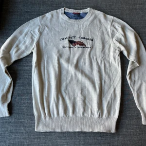 Vit bomullströja från Gant - 📦 Säljer en stilren vit tröja från Gant med broderad text 'GANT 1949' och en amerikansk flagga på framsidan. Tröjan är tillverkad i 100% bomull och har långa ärmar samt ribbade muddar vid ärmslut och nederkant. Perfekt för en avslappnad stil. Storlek M, normal i storleken. Vid frågor, tveka inte att höra av er! ☺️