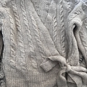 Beige stickad kofta från Zabaione - Säljer en mysig beige stickad kofta från Zabaione med flätmönster och knytband i midjan. Perfekt för kyliga dagar med sin mjuka och varma design. Koftan har långa ärmar och en omlottstil som ger en avslappnad look. Storlek M men känns som S/Xs