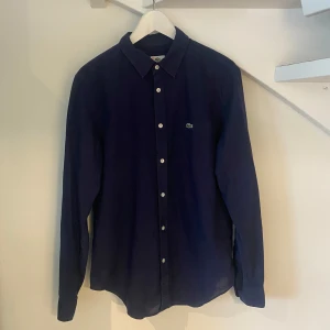 Lacoste skjorta - Jättefin skjorta från märket Lacoste i färgen mörkblå😊 skicket på skjortan är helt fantastiskt och är som nya🤩 nypris runt 1400kr vårt pris 349kr!