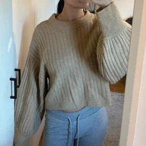 Beige ribbad stickad tröja från Gina tricot - Säljer en mysig beige stickad tröja med ribbad struktur. Tröjan har en croppad passform och långa ärmar med breda muddar. Perfekt för kyliga dagar eller sena sommarkvällar!
