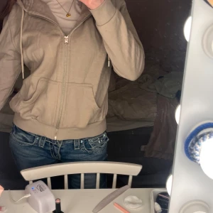 Beige hoodie med dragkedja - Säljer en beige hoodie med dragkedja och huva. Tröjan har en normal passform och är tillverkad i ett mjukt material. Perfekt för en avslappnad stil.