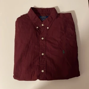 Vinröd skjorta från Polo Ralph Lauren - Vinröd bomullsskjorta med button-down krage från Polo Ralph Lauren. Knappslå, långa ärmar med manschetter. Broderad logotyp på bröstet. Köpt 2023 från johnells för 1600kr, använd 2-3 gånger och är i nyskick.