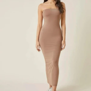 Tubklänning - Snygg beige axelbandslös klänning med tight passform och slits bak. Sitter perfekt på kroppen och superfin till sommaren! Stretchig så passar nog upp till M/L. Säljer då den inte kommer till användning. Skriv för fler bilder!