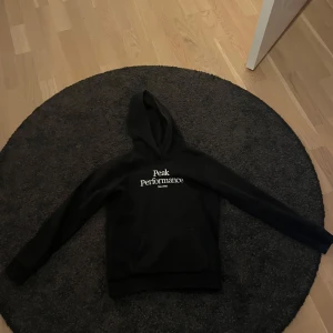 Svart hoodie från Peak Performance - Säljer en stilren svart hoodie från Peak Performance med vit logga på bröstet. Perfekt för en avslappnad stil. Den har en klassisk huva och långa ärmar.