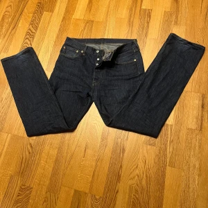 Levis 501 jeans - Säljer ett par klassiska Levis 501 jeans i mörkblå denim. De har en rak passform och knappar i gylfen. Perfekta för en tidlös stil. Skriv vid funderingar, svarar snabbt🤝