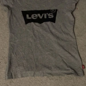 Grå t-shirt från Levi's - Säljer en klassisk grå t-shirt från Levi's med deras ikoniska logga i svart på bröstet. Storleken är 2 storlekar större än den röda Levis tröjan, så sitter lite mer läsare och inte så tight. Perfekt för en avslappnad stil. T-shirten har korta ärmar och är tillverkad i mjuk bomull.