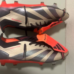Adidas Predator fotbollsskor - Snygga Adidas Predator fotbollsskor i beige och svart med röda detaljer. Skorna har en modern design med snörning och är perfekta för fotbollsplanen. De har en slitstark sula med dobbar för optimalt grepp. Priset kan diskuteras. Använda 3 gånger. 