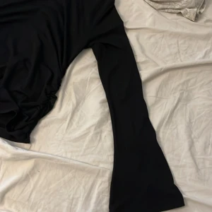 Svart långärmad topp från Gina Tricot - Snygg svart långärmad topp från Gina Tricot med rynkade detaljer på sidorna. Perfekt för en stilren look. Tillverkad i ett mjukt och bekvämt material.