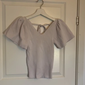 Vit/ljusrosa ribbad topp med knytning i ryggen från only  - Säljer en söt ljuslila ribbad topp med korta puffärmar och v-ringning. Toppen har ett knytband i ryggen som ger en fin detalj. Perfekt för en stilren och bekväm look.
