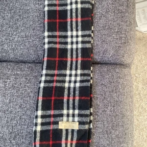 Rutig halsduk från Burberry - Snygg rutig halsduk från Burberry i klassiska färger. Den har ett stilrent mönster i svart, vit och röd.  Perfekt för det kommande vår vädret